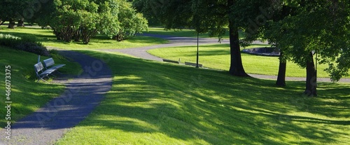 Fényképezés Green meadow with shadow of trees and benches on footpath at public park green g
