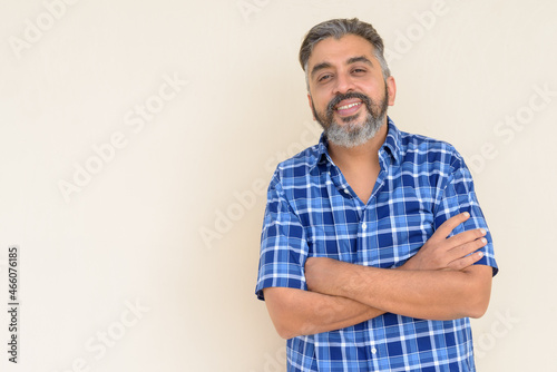 Portrait of bearded Indian businessman smiling against plain background