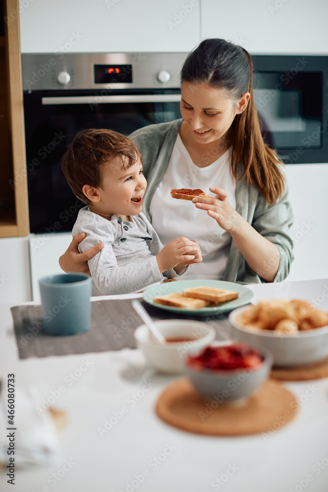 Happy mother feeds her son during breakfast at dining table.