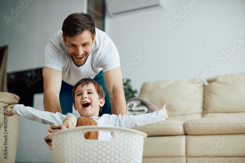 Fotografie Carefree boy has fun while father is pushing him in laundry basket around the house