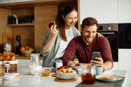 Happy couple use mobile phone while having breakfast together in the morning.