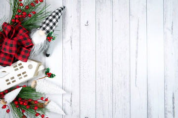 Christmas Farmhouse style background styled with red plaid bows, village houses and gnomes. against a white wood background. Negative copy space.