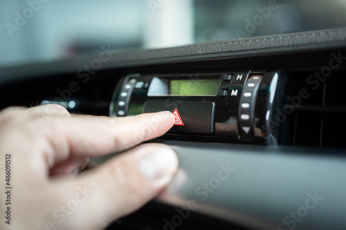 Action of driver is pressing on the emergency signal switch during accident or breakdown situation, calling for help. Transportation scene photo. Close-up and selective focus at the switch's part.