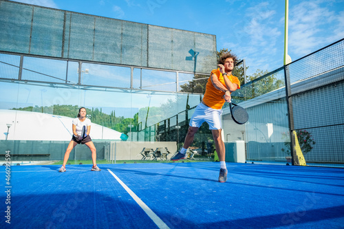Mixed padel match in a blue grass padel court - .Beautiful girl and handsome man playing padel outdoor