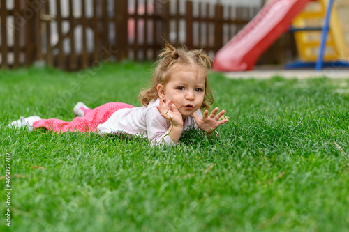 Portrait of a girl lying on the grass of a playground looking at the camera.