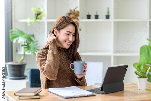 Free Download Beautiful young Asian woman smiling holding a coffee mug and laptop, tablet working at the office.. - GFXLoad