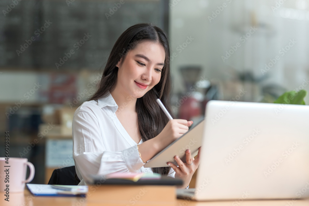 Happy young Asian businesswoman working on laptop and taking notes In office. Happy young Asian businesswoman working on laptop and taking notes In office.