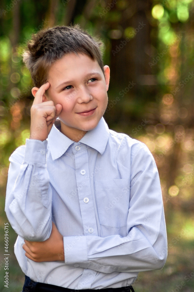 Portrait of a schoolboy looking thoughtfully to the side, against a blurry background of green trees. Portrait of a schoolboy looking thoughtfully to the side, against a blurry background of green trees.