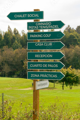 green signpost indianco the directions of the golf course, with a street in the background 