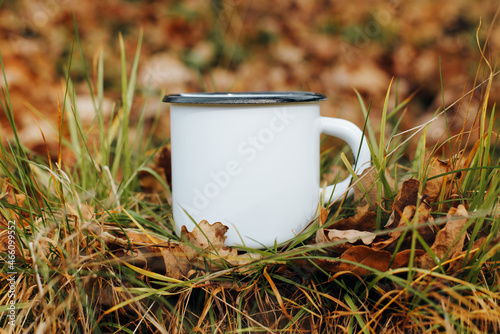 Metallic white mug mock-up. Hike camping or travel template concept. Close-up enamelled clean mug standing on autumn foliage outdoors