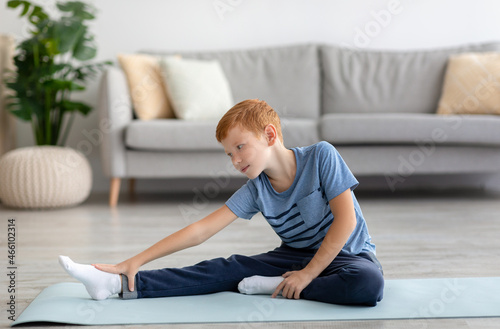 Cute redhead boy stretching on fitness mat at home