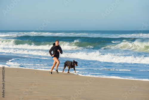 beautiful young athletic woman running with her dog on the beach