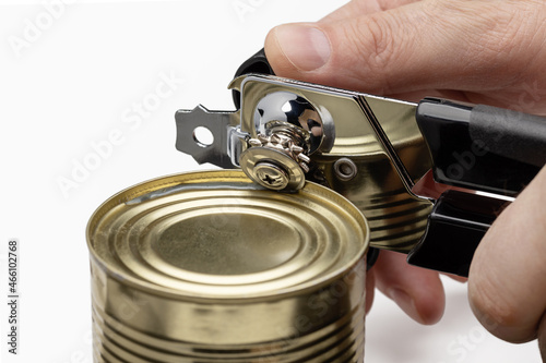 In men's hands a can opener opening a can of food. Kitchen utensils. photo