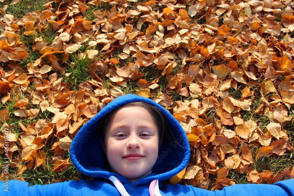Top view portrait of happy child having fun outdoor in autumn park. Smiling kid lying on green grass against yellow leaves blurred background. High quality photohappy little girl, cute little girl Top view portrait of happy child having fun outdoor in autumn park. Smiling kid lying on green grass against yellow leaves blurred background. High quality photohappy little girl, cute little girl