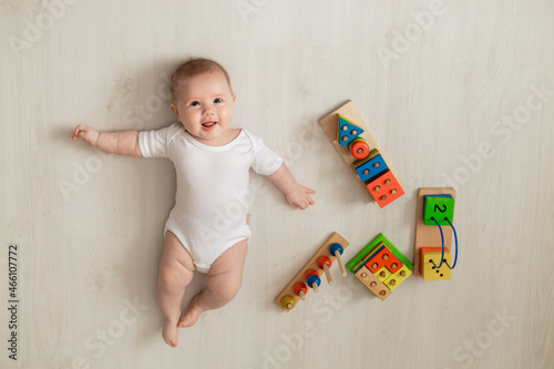 Foto cheerful newborn baby in a white bodysuit lies on his back on the floor and plays with educational toys
