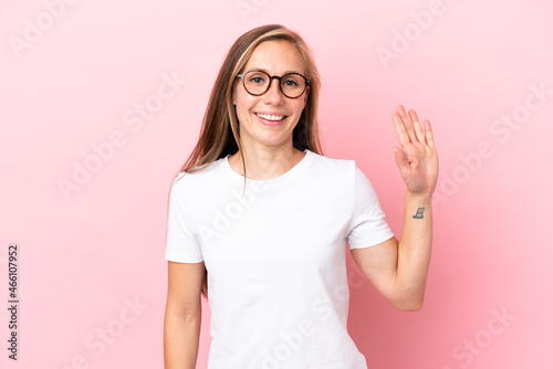 Young English woman isolated on pink background saluting with hand with happy expression