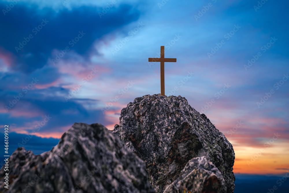 Silhouettes of crucifix symbol on top rock mountain with bright sunbeam on the colorful sky background