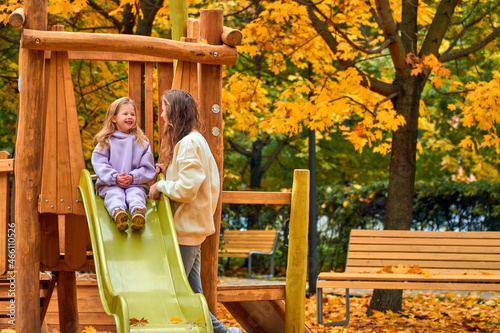 Mom and daughter on playground in autumn. family play on wooden slide. New home babysitter. park for happy family. woman and girl are smile. look at camera. Have fun weekend together. sisters joke