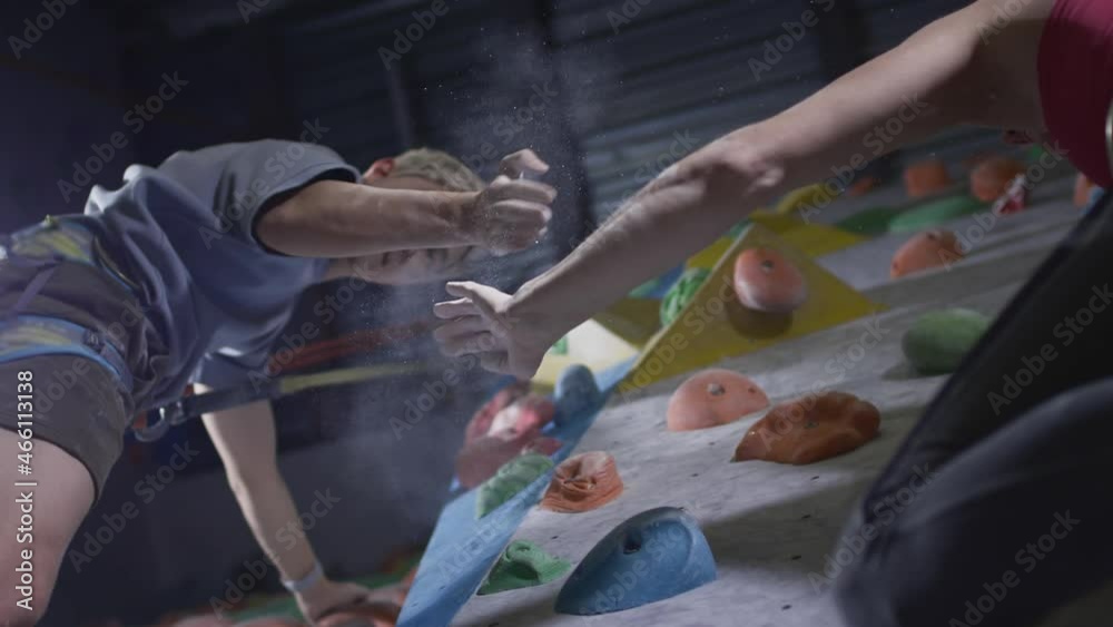 Sport girl and athletic man climbers give five on the climbing wall in the gym. Uses a safety rope and clothing on the bouldering wall. Grabs hands on stones and ledges. Success and victory. Sport girl and athletic man climbers give five on the climbing wall in the gym. Uses a safety rope and clothing on the bouldering wall. Grabs hands on stones and ledges. Success and victory.