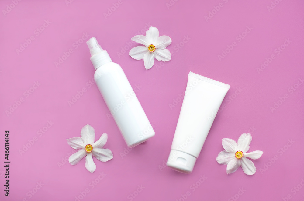 A tube and a jar with a white spray and white narcissus flowers on a pink background A tube and a jar with a white spray and white narcissus flowers on a pink background