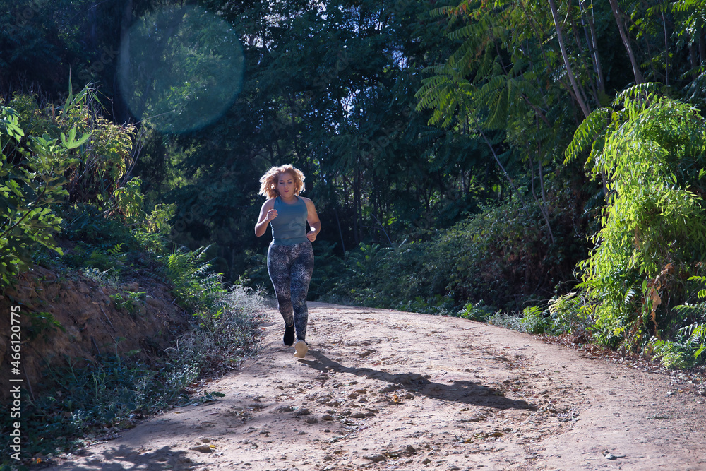 Young blonde woman in sportswear running cross-country through the mountains on a nature trail. Concept, running, trailrunning, fitness, exercise, curvy girl.