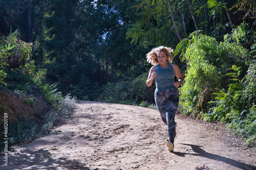 Young blonde woman in sportswear running cross-country through the mountains on a nature trail. Concept, running, trailrunning, fitness, exercise, curvy girl. photo