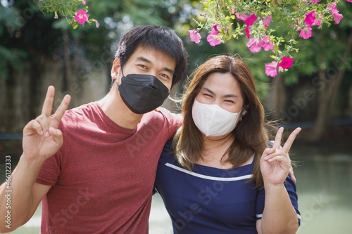 asian couple wearing protection face mask hand sign victory standing outdoor photo