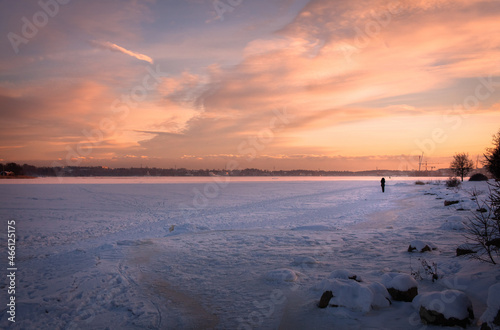 Winter sunset over the frozen sea. A silhouette of a woman walking on ice. 