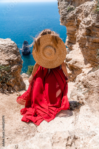 Photos A girl with loose hair in a long red dress descends the stairs between the yellow rocks overlooking the sea