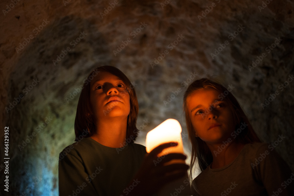 Brave little children exploring dark old castle. Courageous boy holding candle in dark tunnel, girl standing behind him. Childhood, nature, fantasy concept Brave little children exploring dark old castle. Courageous boy holding candle in dark tunnel, girl standing behind him. Childhood, nature, fantasy concept