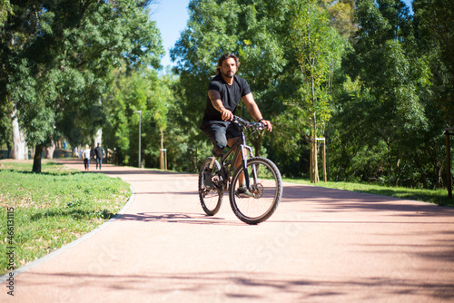 Person with disability riding bicycle. Curly man with mechanical leg exercising in park on sunny day. Sport, disability concept