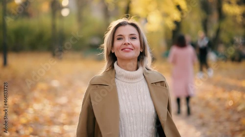 Attractive mature blond woman walking down the park turns around with flying hair and looking at the camera outdoors Happy relaxed female walking on the autumn park enjoying beautiful time photo