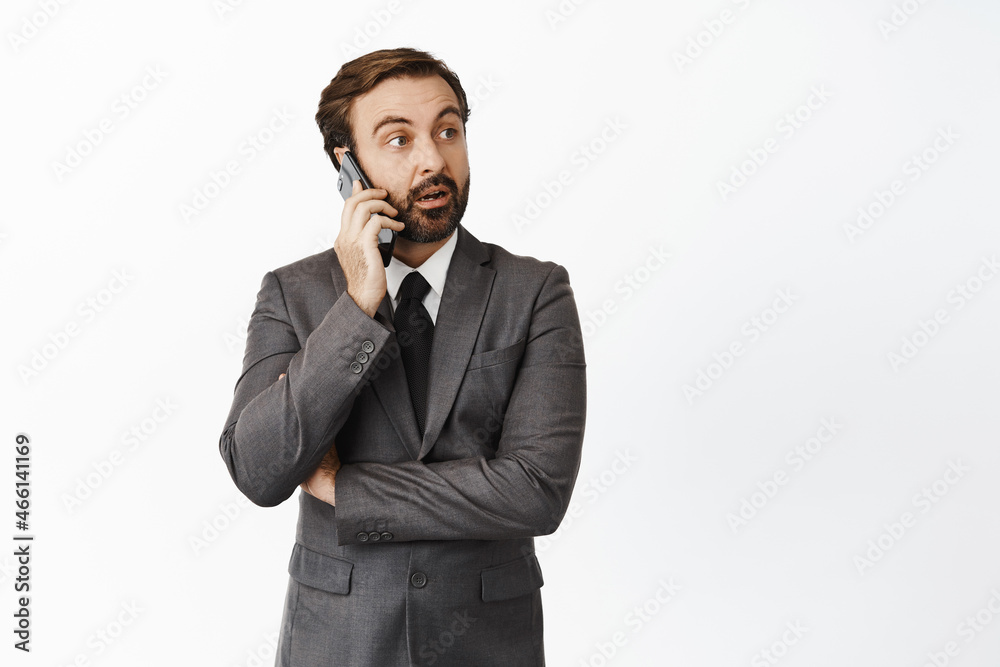 Businessman talking on cellphone and looking surprised at promotion text, advertisement on right side, standing over white background Businessman talking on cellphone and looking surprised at promotion text, advertisement on right side, standing over white background