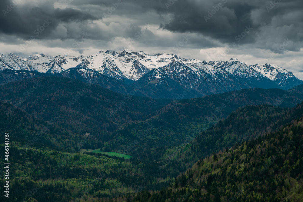 Snow covered Bavarian Alps with dramatic dark clouds, green forest at Jachenau near Lake Walchensee, Bavaria.