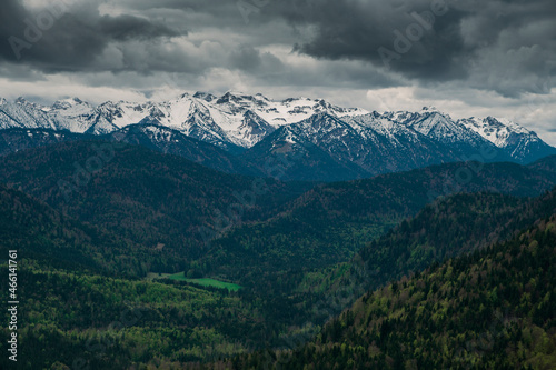 Snow covered Bavarian Alps with dramatic dark clouds, green forest at Jachenau near Lake Walchensee, Bavaria.
