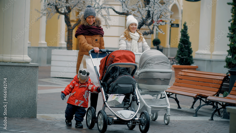Two young attractive mothers with their babies walk in city center