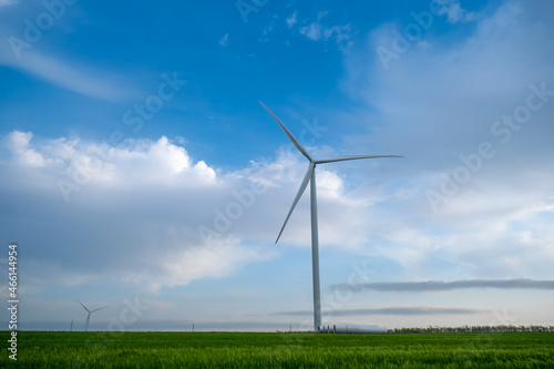 Wind power plant on agricultural field against the background of blue sky with clouds.