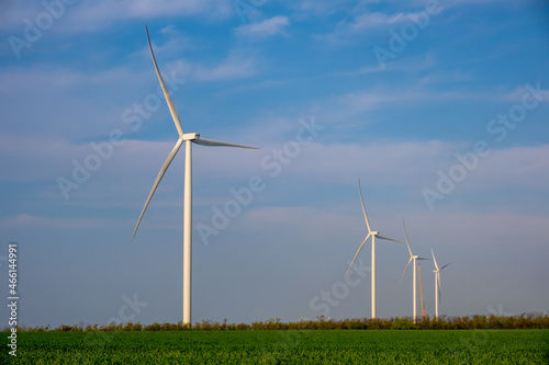 Wind power plant on agricultural field against the background of blue sky with clouds.