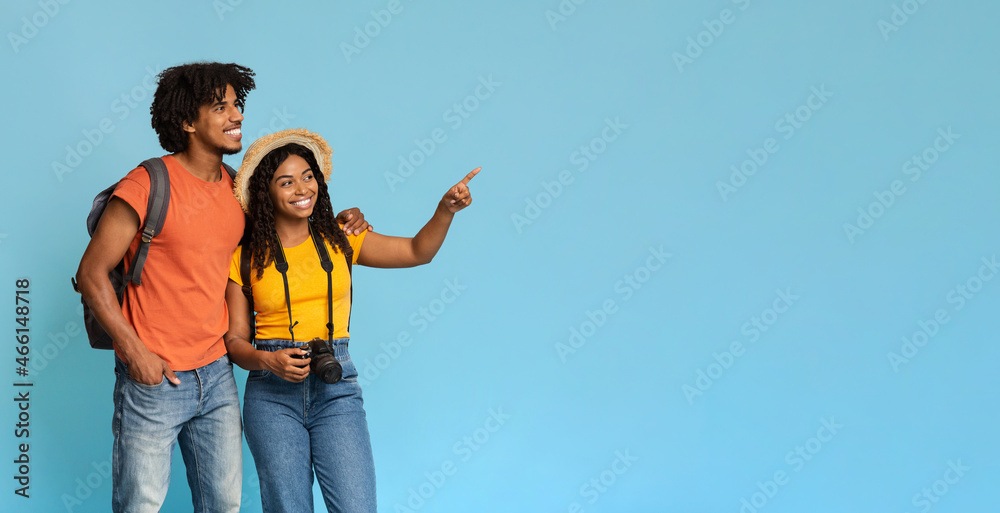 Happy black couple tourists with backpacks pointing at copy space Happy black couple tourists with backpacks pointing at copy space