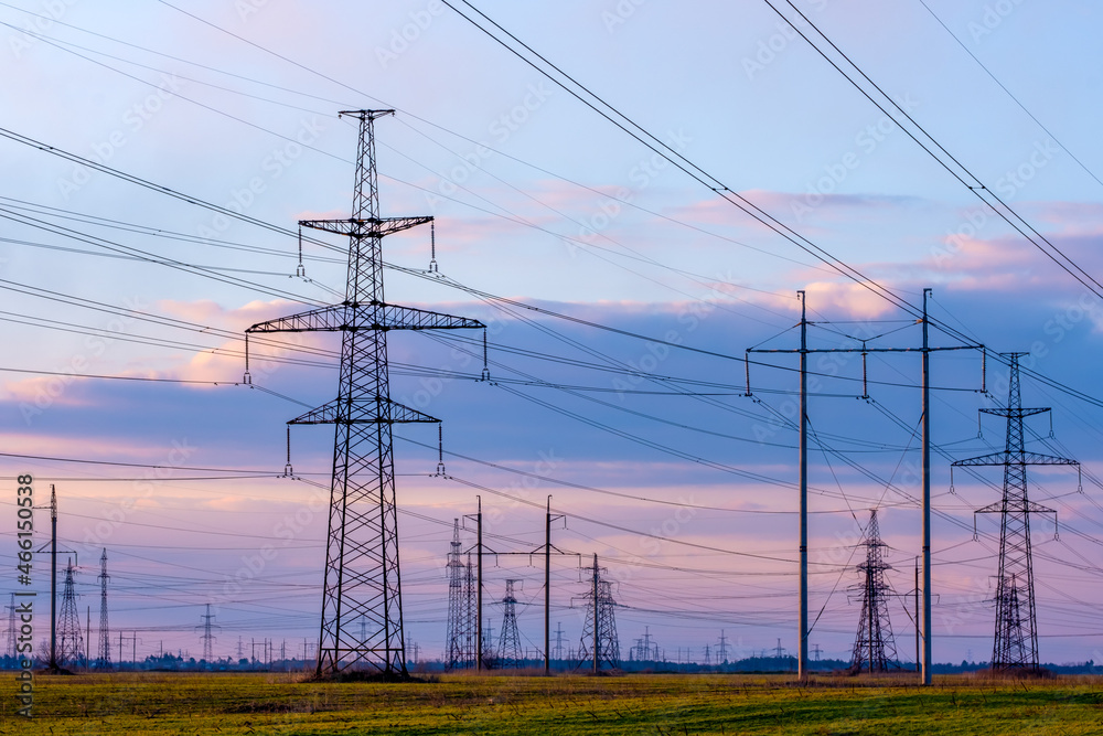 High-voltage power lines on the background of the evening sky. Transmission of electricity by means of poles through agricultural land.