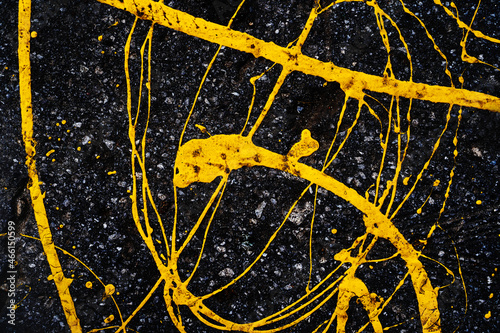 Yellow paint spilled onto the dark asphalt. Abstract composition with chaotic lines and drops. Flat frame