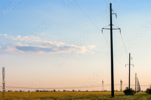 High-voltage power lines on the background of the evening sky. Transmission of electricity by means of poles through agricultural land.