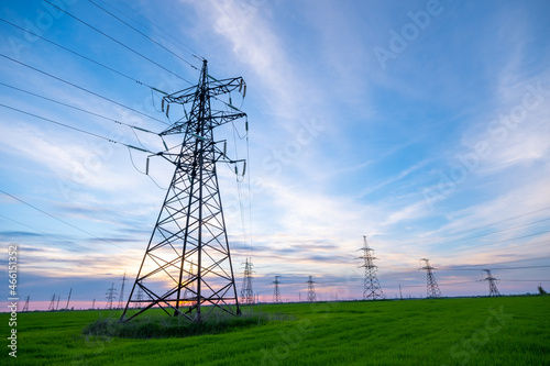 High-voltage power lines on the background of the evening sky. Transmission of electricity by means of poles through agricultural land.