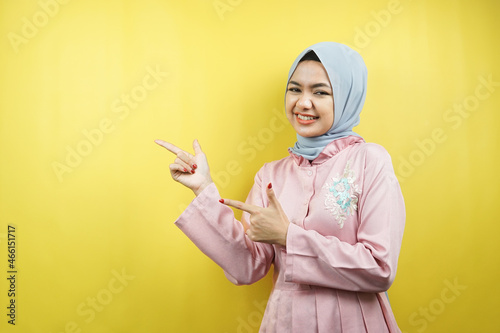 Cheerful beautiful young muslim woman, with hand pointing at empty space, promoting something, isolated © MunirSr