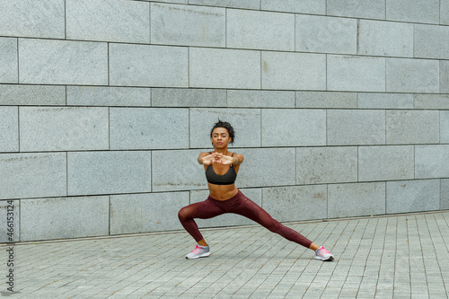 Young flexible woman in top and leggings does sports exercises for arms training near light grey stone wall