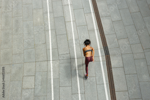 Young biracial woman in stylish sportswear runs along empty stadium track upper view. Development and achievement concept