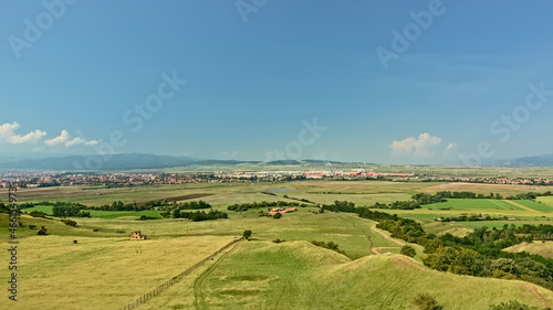 Transylvanian landscape with green fields with and a city and mountains in the distance on a sunny day with clear blue sky  view from above ffrom Rapa Rosie  Romania 