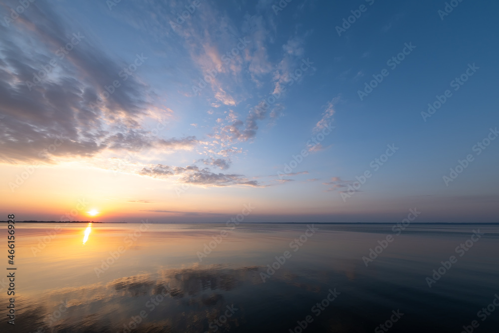 Beautiful, colorful sunset, sunrise over a wide river. Twilight rays and clouds reflected in the calm water. 