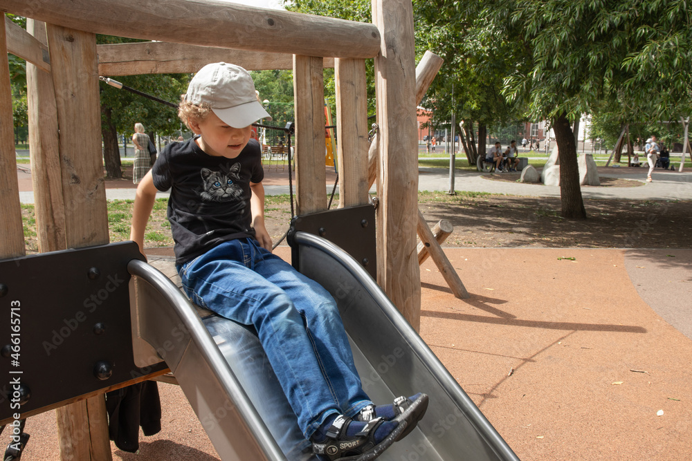 A primary school boy is playing in the playground. The boy sits on a children's slide. The photo A primary school boy is playing in the playground. The boy sits on a children's slide. The photo