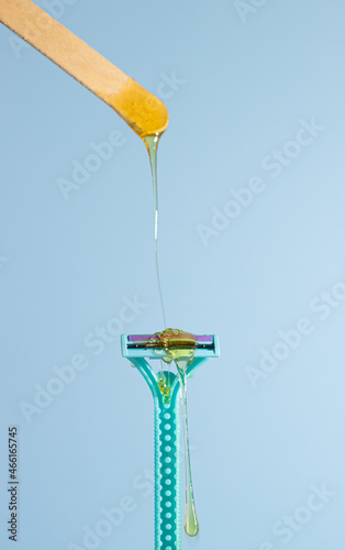 Sugar paste for hair removal against a razor. Sugaring paste drips on a razor on a blue background. The concept of epilation, spa, body care.